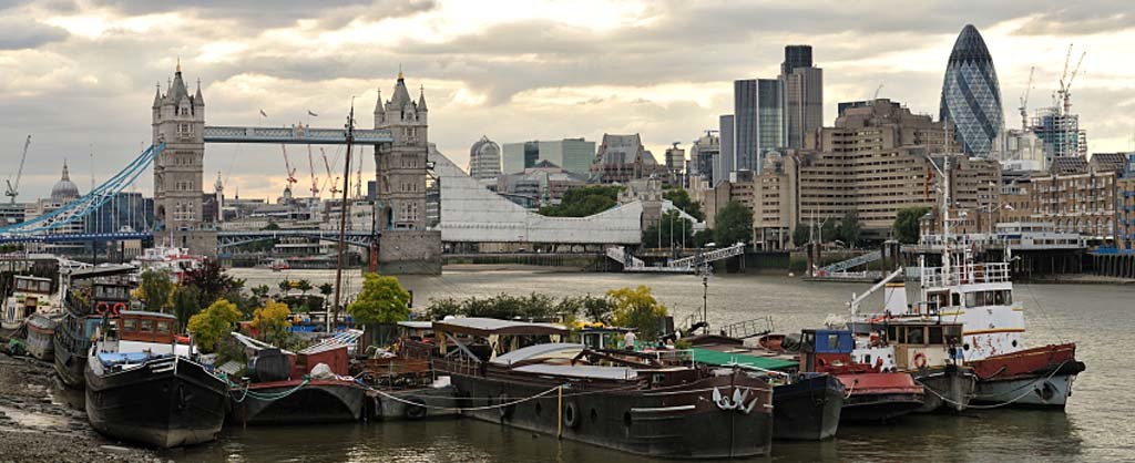 Houseboats moored on the south bank of the River Thames, Bermondsey, Southwark, London, England, UK, with Tower Bridge, being refurbished for the Olympics, in tne background, and a dramatic stormy sky at the end of the day